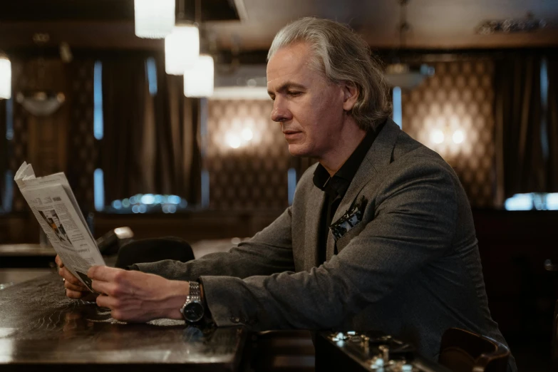 a man sitting at a table reading a newspaper, a portrait, unsplash, photorealism, david spade, elegantly dressed, jimmy page, sitting at the bar