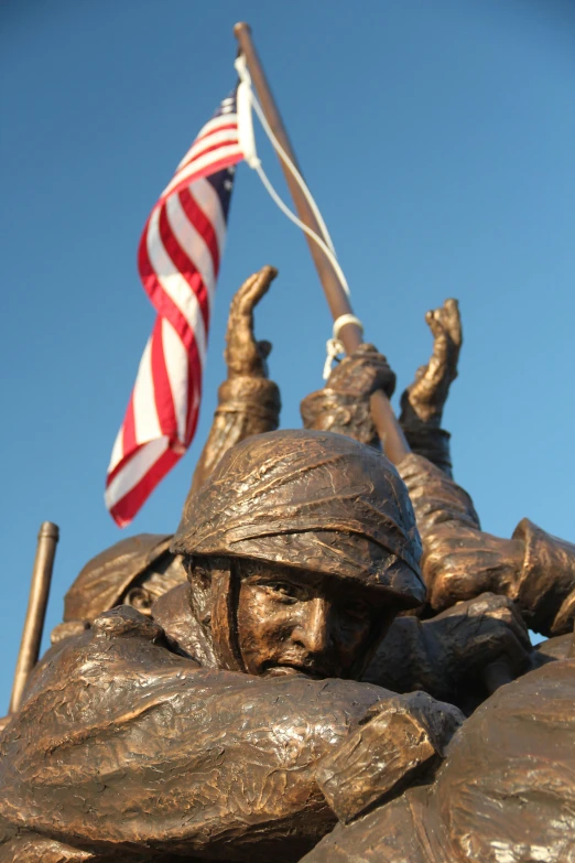 a statue of a soldier holding an american flag, center of image, close - up of the faces, blue sky, warmly lit