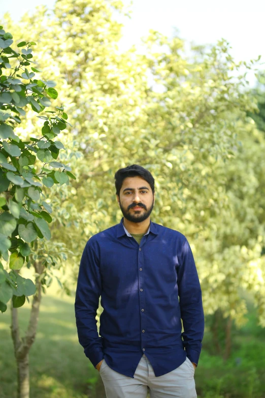 a man standing in front of a tree, by Riza Abbasi, wearing a light blue shirt, lush environment, on clear background, an afghan male type