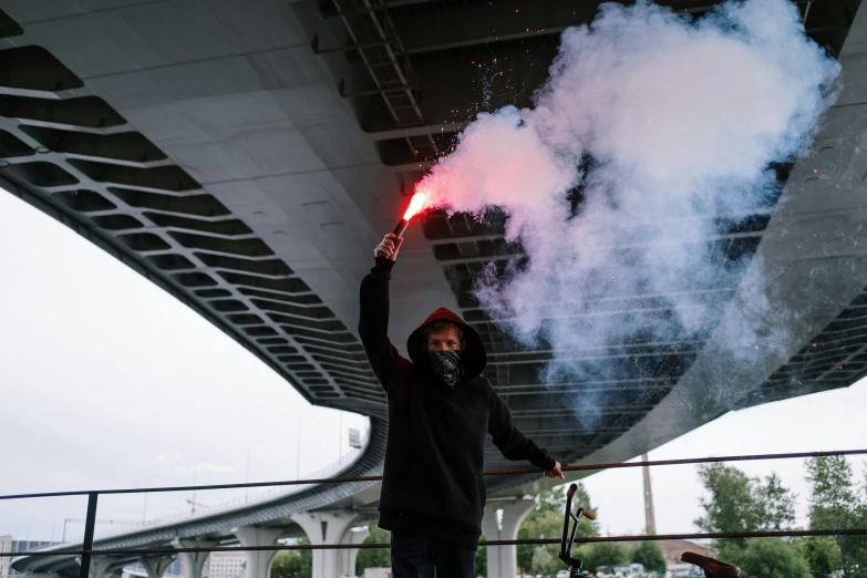 a man holding a red light up in the air, a picture, unsplash contest winner, graffiti, smokey cannons, overpass, red and black cape and hoodie, seattle completely wasted away