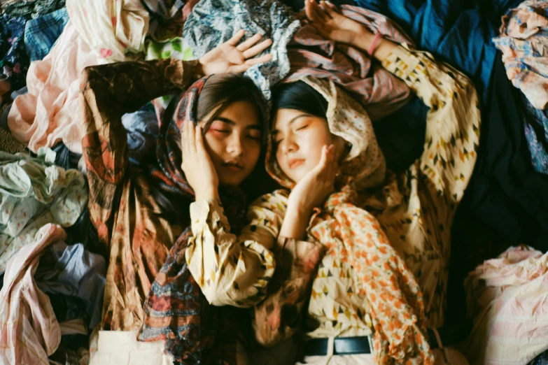 a couple of women laying on top of a pile of clothes, by irakli nadar, trending on pexels, wearing a head scarf, patterned clothing, film photo, mingchen shen