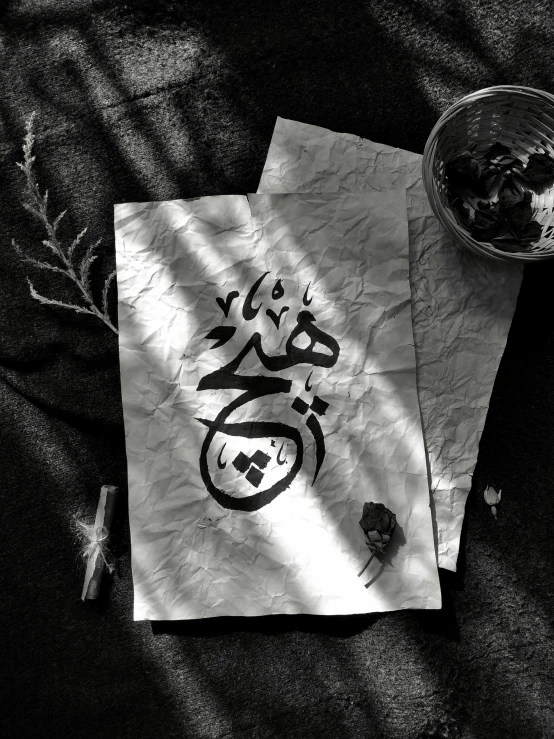 a piece of paper sitting on top of a table, an album cover, by Ahmed Yacoubi, unsplash, hurufiyya, japanese calligraphy, black and white color aesthetic, islamic art, sigil