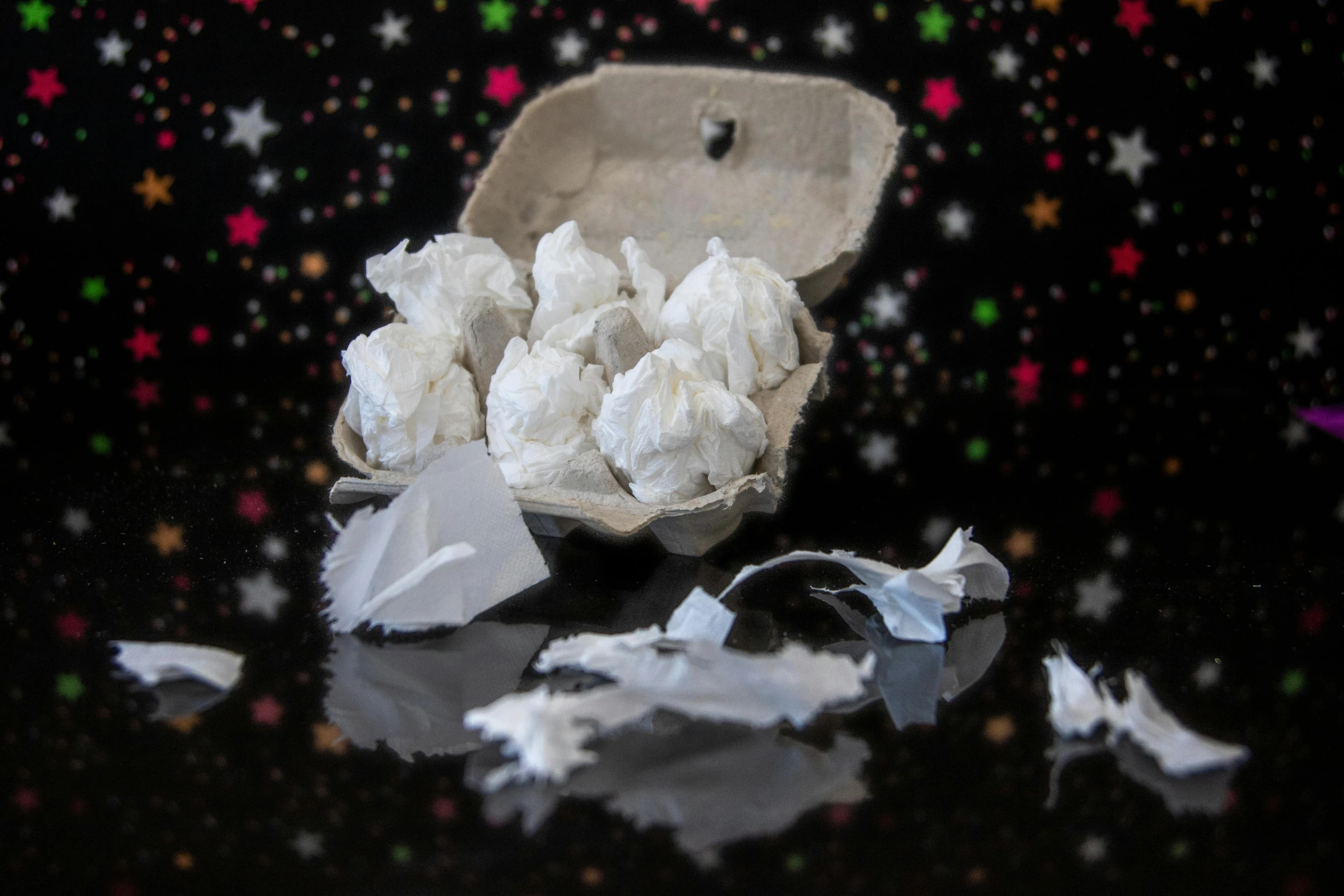 a broken egg carton sitting on top of a table, a marble sculpture, inspired by Tracey Emin, pexels, conceptual art, falling stars, tribbles, with a black background, candy treatments