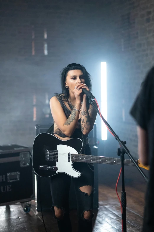 a woman singing into a microphone while holding a guitar, a tattoo, performing a music video, 2019 trending photo, woman with black hair, epk