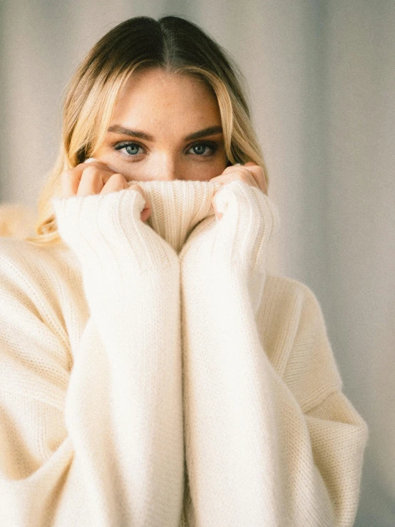 a woman covering her face with her hands, a character portrait, by Robbie Trevino, trending on unsplash, wearing a white sweater, portrait of margot robbie, wearing an oversized sweater, product introduction photo