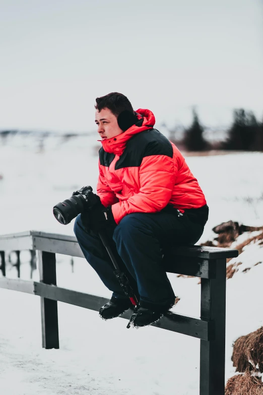 a person sitting on a bench in the snow, with nikon cameras, black and red jacket, avatar image, profile photography