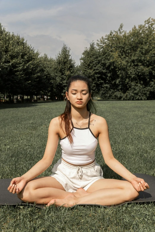 a woman sitting on a yoga mat in a park, a statue, trending on pexels, south east asian with round face, bralette, 5k, calm face