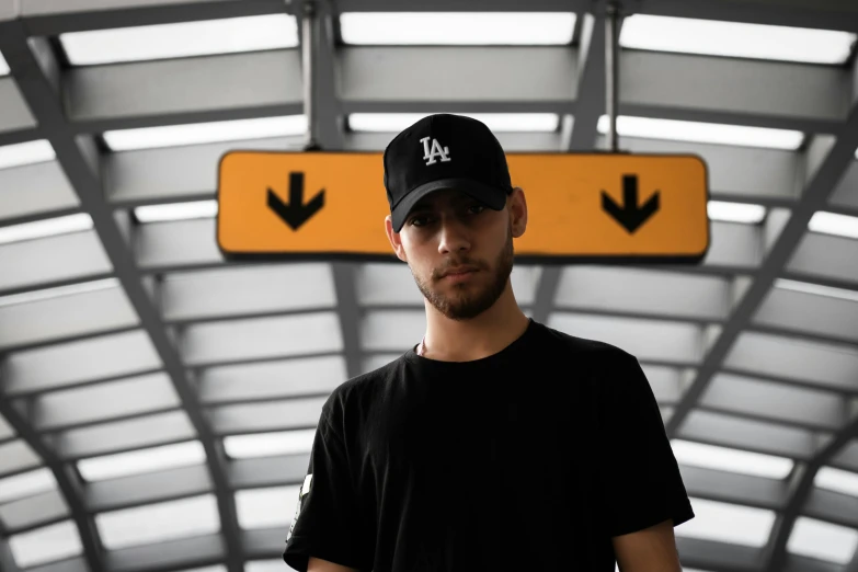 a man that is standing in front of a sign, baseball cap, black. airports, streetwear, discord profile picture