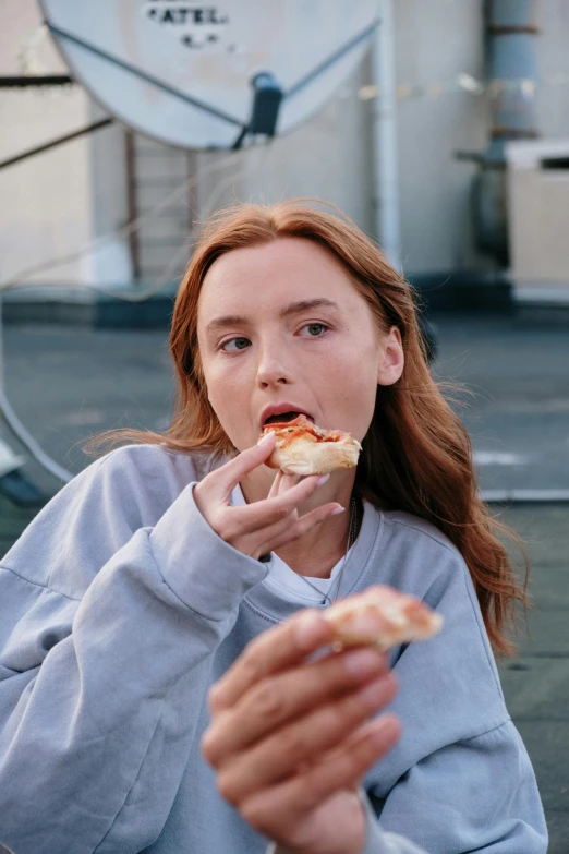 a woman is eating a slice of pizza, trending on pexels, renaissance, eleanor tomlinson, on rooftop, very light freckles, wearing sweatshirt