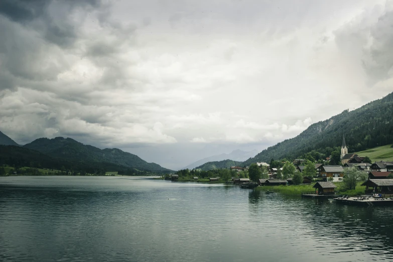 a body of water surrounded by mountains under a cloudy sky, austrian architecture, fan favorite, promo, waterfront houses