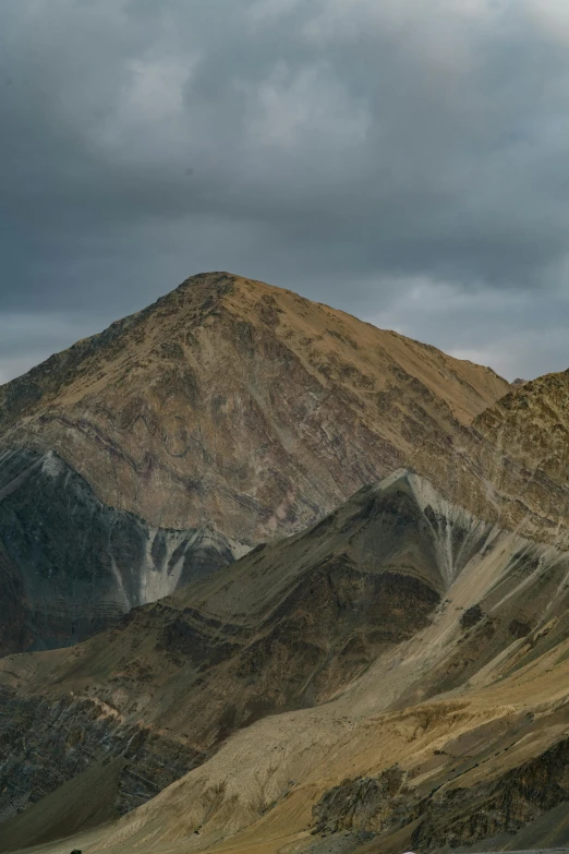 a car driving down a road with mountains in the background, by Muggur, trending on unsplash, les nabis, geological strata, dark grey and orange colours, sitting atop a dusty mountaintop, uttarakhand