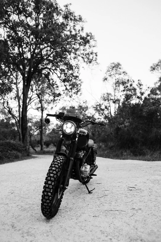 a black and white photo of a motorcycle parked on a dirt road, a black and white photo, unsplash, medium format, front, made of tar, stylish pose