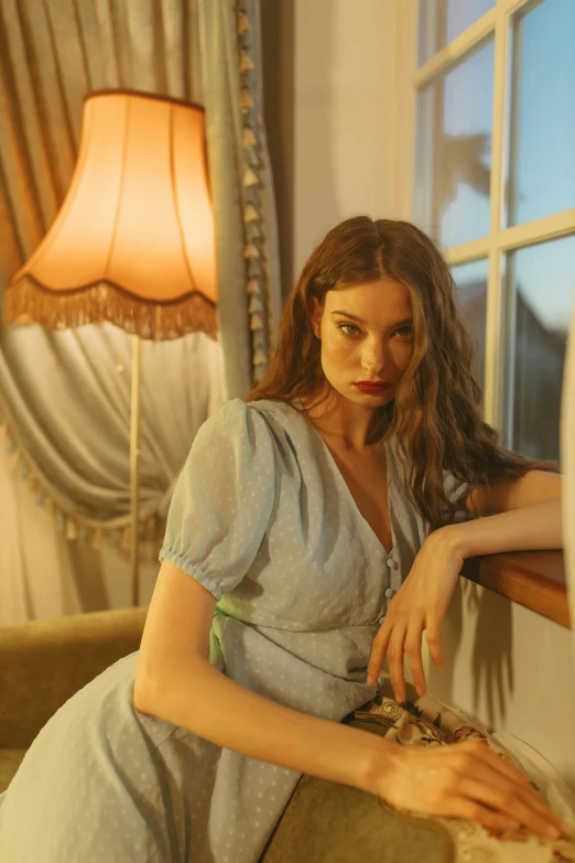 a woman sitting on a couch next to a window, a portrait, inspired by Elsa Bleda, trending on pexels, renaissance, pale blue outfit, 8 k sensual lighting, vintage clothing, summer night