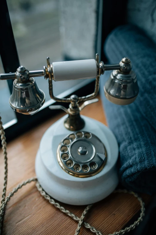 a white telephone sitting on top of a wooden table, silver with gold accents, monocle, up-close, worn