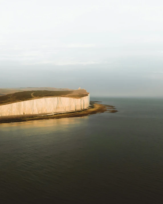 a large body of water next to a cliff, an album cover, by Daniel Seghers, pexels contest winner, cliffs of dover, ignant, farming, brown