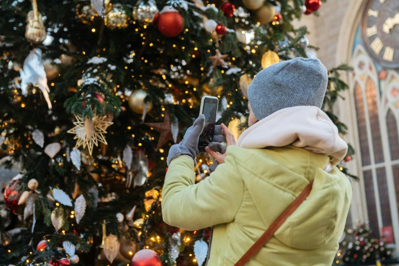 a woman taking a picture of a christmas tree, by Julia Pishtar, pexels, square, tourism, dressed in a beautiful, a cozy