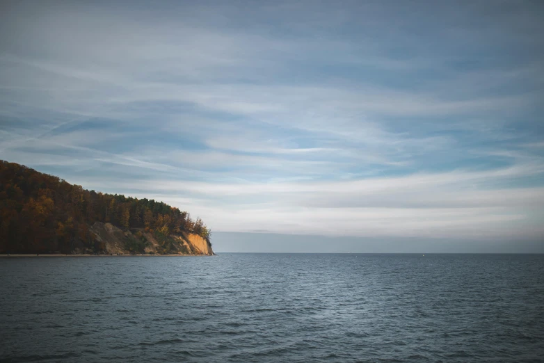 a body of water with a hill in the background, a picture, by Jesper Knudsen, unsplash, romanticism, coastal cliffs, espoo, brown, blue gray