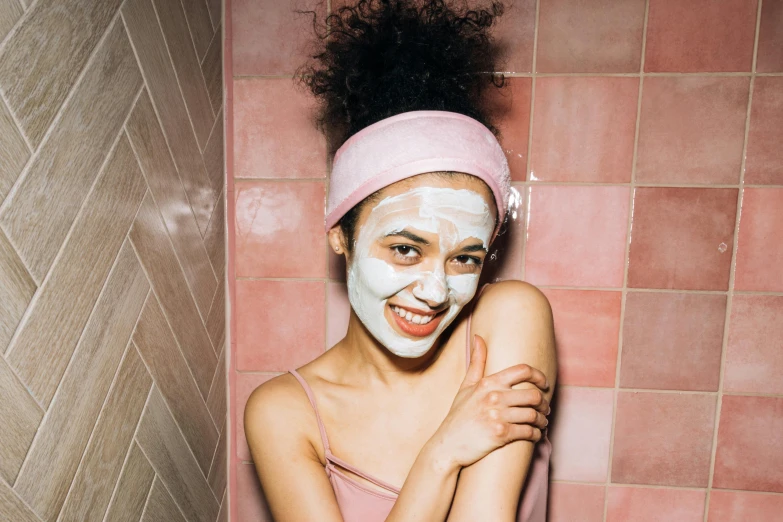 a woman with a face mask in a bathroom, a portrait, by Julia Pishtar, trending on pexels, pastel pink skin tone, smiling mask, manuka, olive skinned