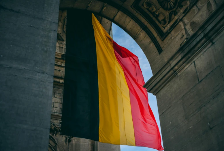 a flag hanging from the side of a building, by Julia Pishtar, pexels contest winner, renaissance, belgium, red yellow black, language, an archway