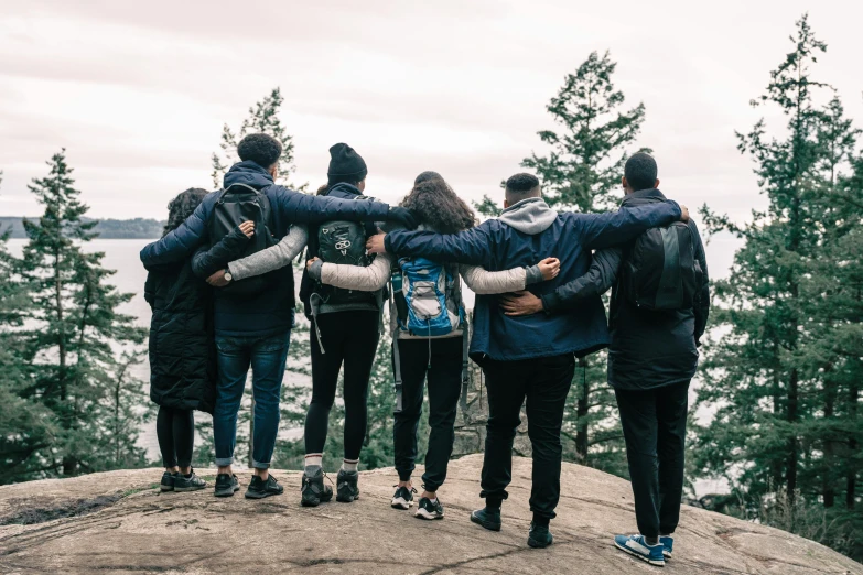 a group of people standing on top of a rock, wearing jeans and a black hoodie, comforting, whistler, college students