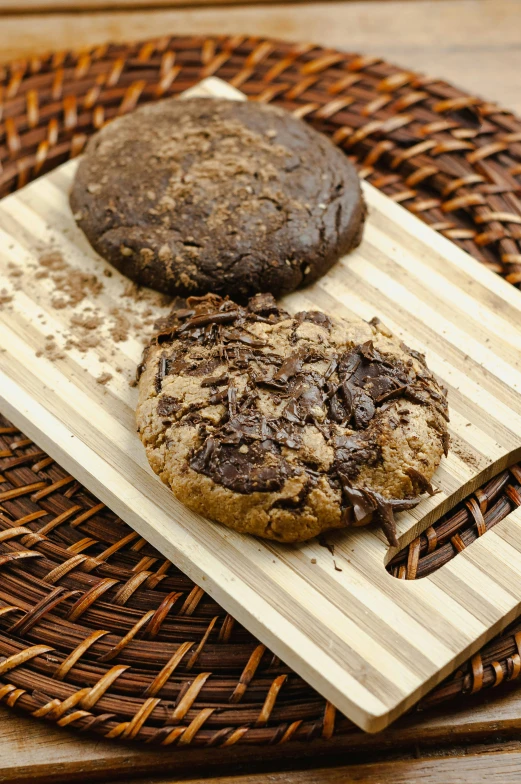 two cookies sitting on top of a wooden cutting board, dark brown, bark, full product shot, fully chocolate