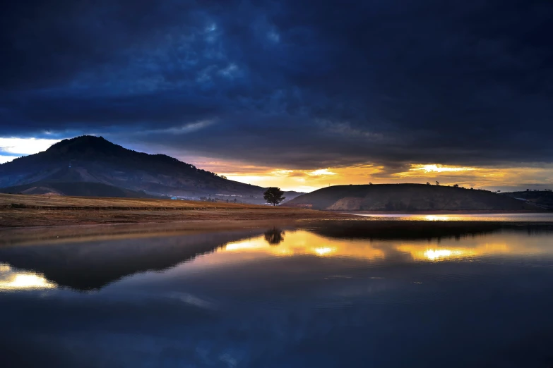 a large body of water with a mountain in the background, inspired by Michal Karcz, unsplash contest winner, hollister ranch, lake reflection, golden and blue hour, moody