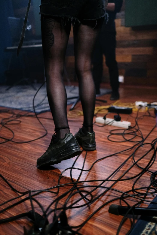 a woman standing on top of a hard wood floor, an album cover, inspired by Nan Goldin, fluxus, has cables, black shoes, live performance, high quality photo