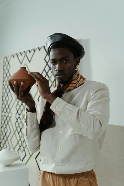 a man standing in a room holding a bowl, inspired by Afewerk Tekle, trending on unsplash, afrofuturism, wearing turtleneck, wearing cylinder hat, white vase, somali attire