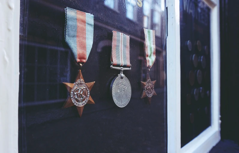 three medals hanging on a wall in front of a window, by Jessie Algie, pexels contest winner, award winning shopfront design, world war ii military style, metal speculars, glass - reflecting - stars