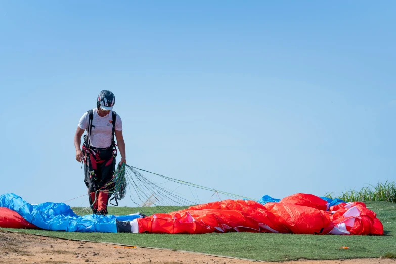 a man standing next to a parachute on top of a field, red and blue garments, aero dynamic, bags on ground, looking onto the horizon