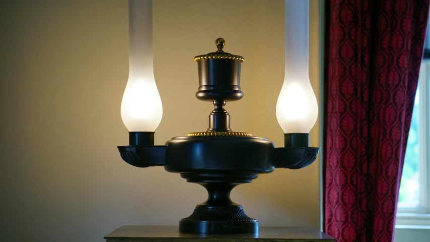 a lamp sitting on top of a table next to a window, inspired by Joseph Wright of Derby, romanticism, symmetric lights, gas lighting, closeup - view, bronze