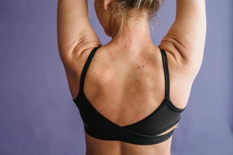 a woman in a black sports bra top holding a tennis racquet, a tattoo, by Carey Morris, trending on pexels, showing her shoulder from back, purple halter top, cysts, manuka