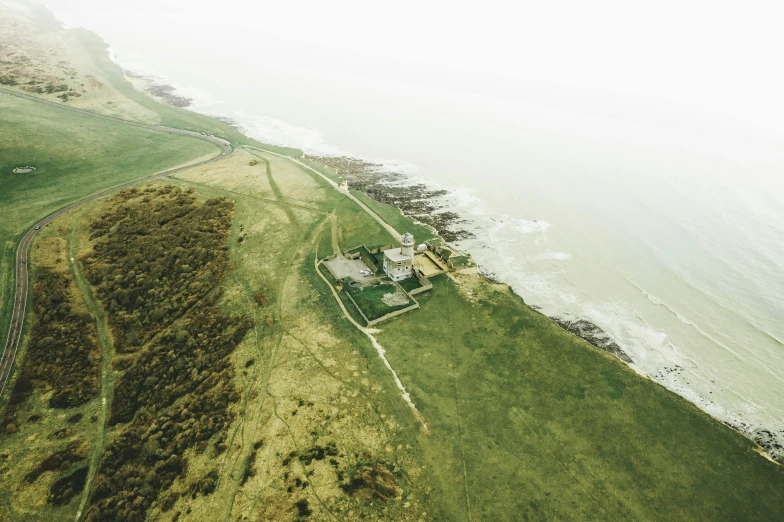 a large grassy field next to a body of water, by Daniel Lieske, unsplash, land art, beachfront mansion, airborne view, lighthouse, high quality image”