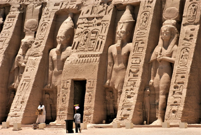 a couple of people that are standing in front of a building, egyptian art, by Thomas Barker, pexels contest winner, buildings carved out of stone, thumbnail, nubian, towering