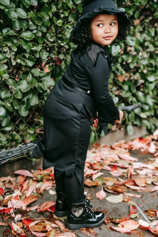 a small child dressed up as a witch, inspired by Kanō Hōgai, unsplash, carrying swords on his back, cassandra cain in satin, curvy accentuated booty, covered in fallen leaves