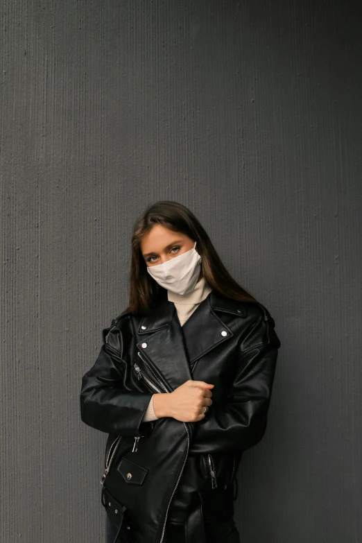 a woman wearing a face mask standing against a wall, trending on pexels, wearing leather jacket, grey backdrop, ilustration, pandemic