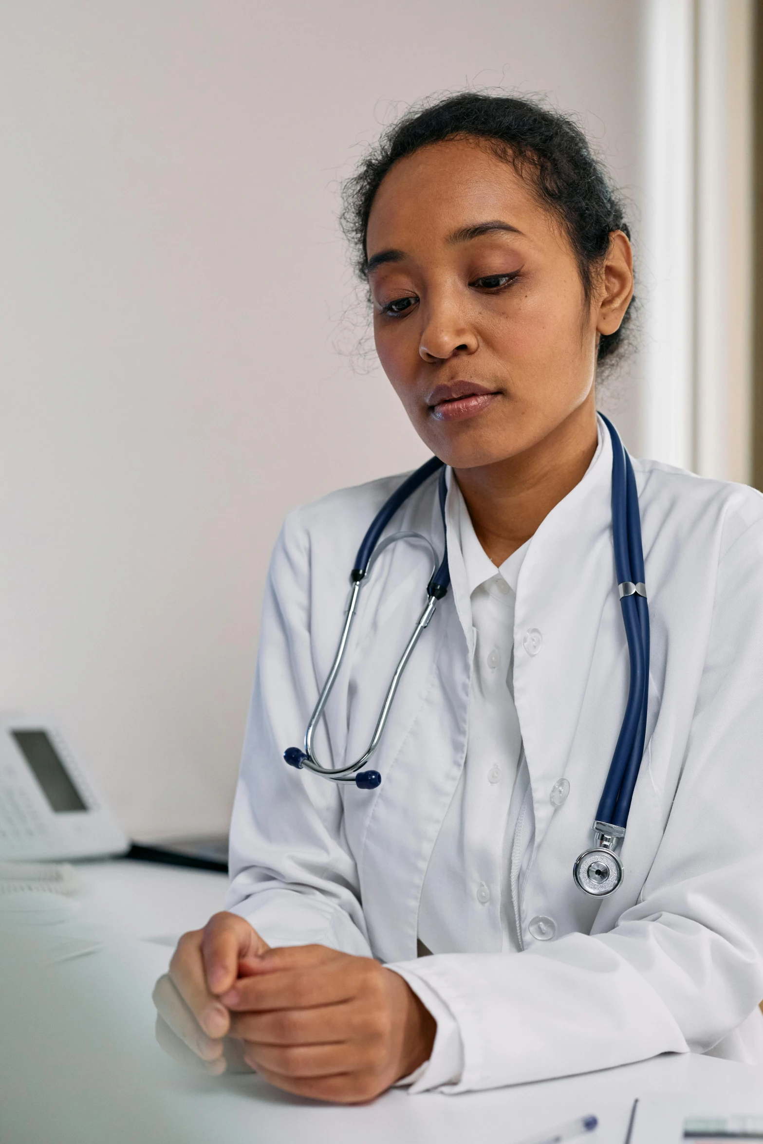 a woman with a stethoscope sitting at a desk, pexels, wearing a white hospital gown, diverse, thumbnail, 1 5 0 4