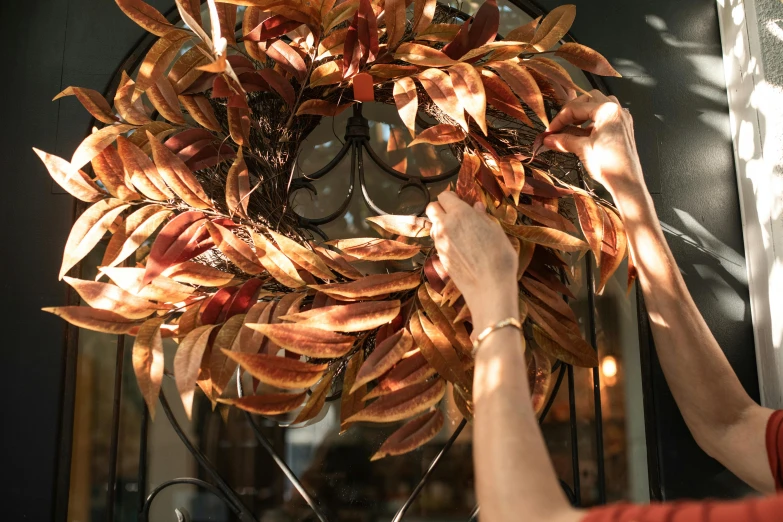 a person hanging a wreath on a door, burnt sienna and venetian red, magnolia leaves and stems, zoomed in, full colour