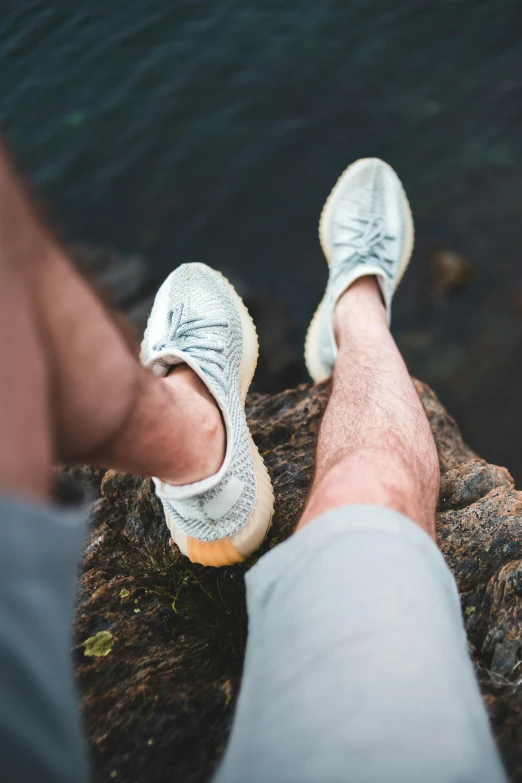 a man sitting on top of a rock next to a body of water, by Jan Tengnagel, trending on unsplash, renaissance, silk shoes, round thighs, pastel blue, grey and silver