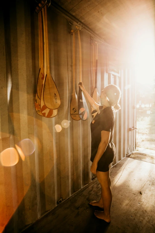 a person standing in a room with guitars hanging on the wall, by Lee Loughridge, unsplash contest winner, happening, late afternoon sun, paddle and ball, inside a shed, holding maracas