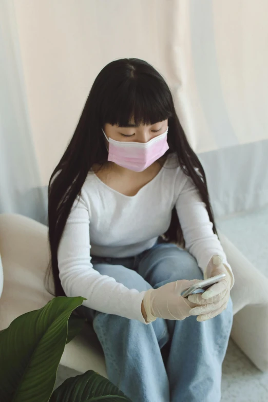 a woman sitting on a couch using a cell phone, surgical mask covering mouth, asian girl with long hair, promo image, sitting in her room