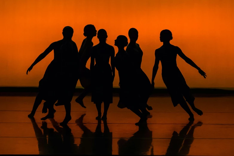 a group of dancers are silhouetted against an orange background, sydney hanson, as photograph, avatar image