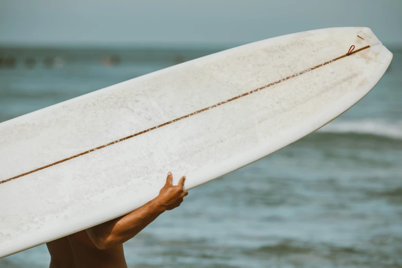 a man holding a white surfboard over his head, pexels contest winner, hand on hip, background image, zoomed in, computer wallpaper