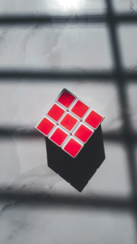 a rubik cube sitting on top of a table, inspired by Ernő Rubik, unsplash, cubo-futurism, white red, square, shot on sony a 7, high - angle