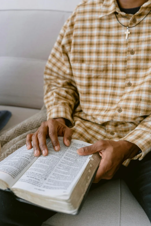 a man sitting on a couch reading a book, by Carey Morris, pexels, renaissance, biblical clothing, wearing a plaid shirt, prayer hands, with yellow cloths