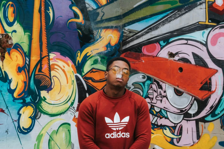 a man standing in front of a wall covered in graffiti, an album cover, pexels contest winner, wearing adidas clothing, red sweater and gray pants, mkbhd, avatar image