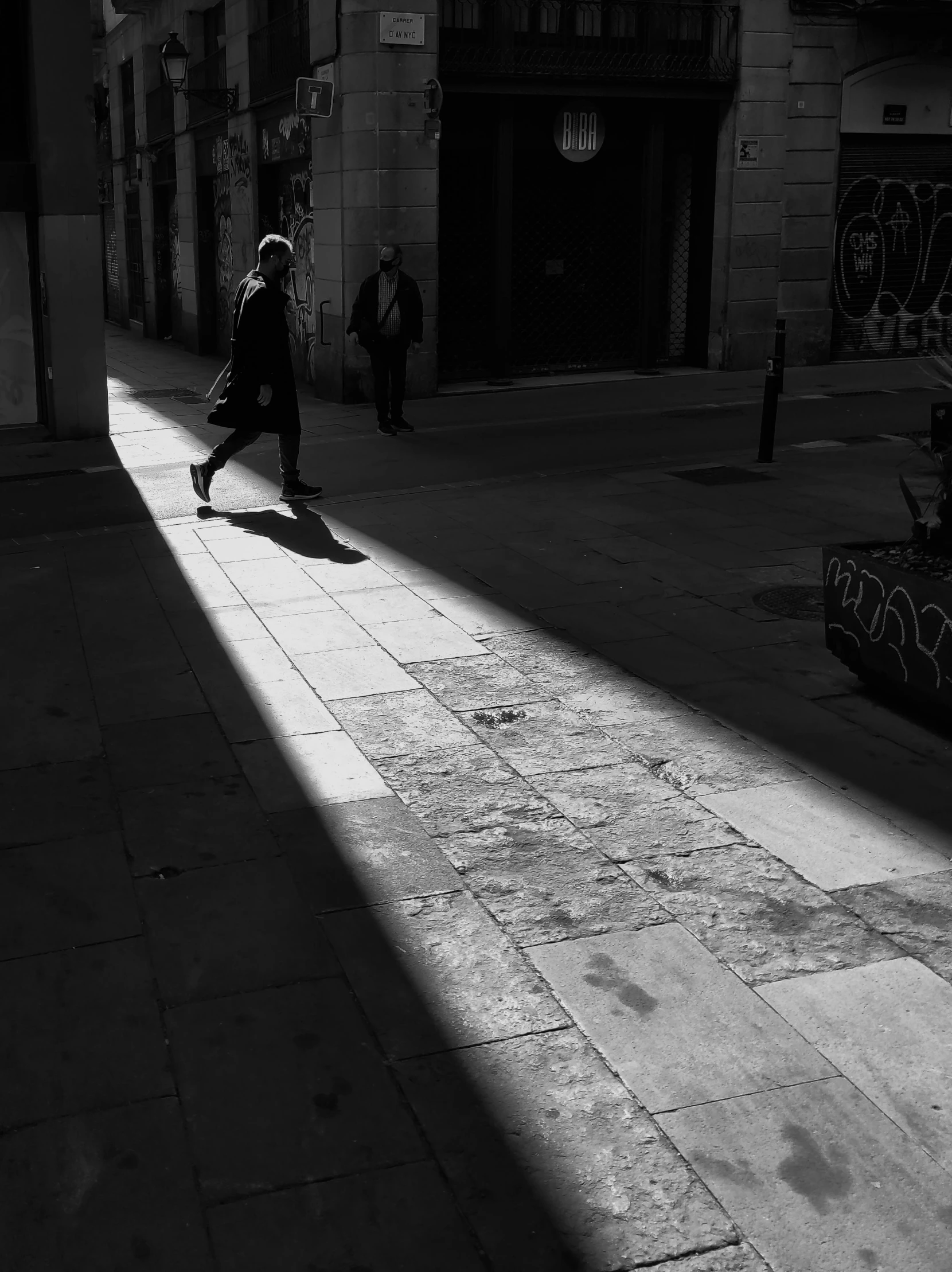 a black and white photo of a person walking down a street, a black and white photo, by Constantine Andreou, light and space, some sun light ray, in barcelona, simone graci, chiaroscuro!!