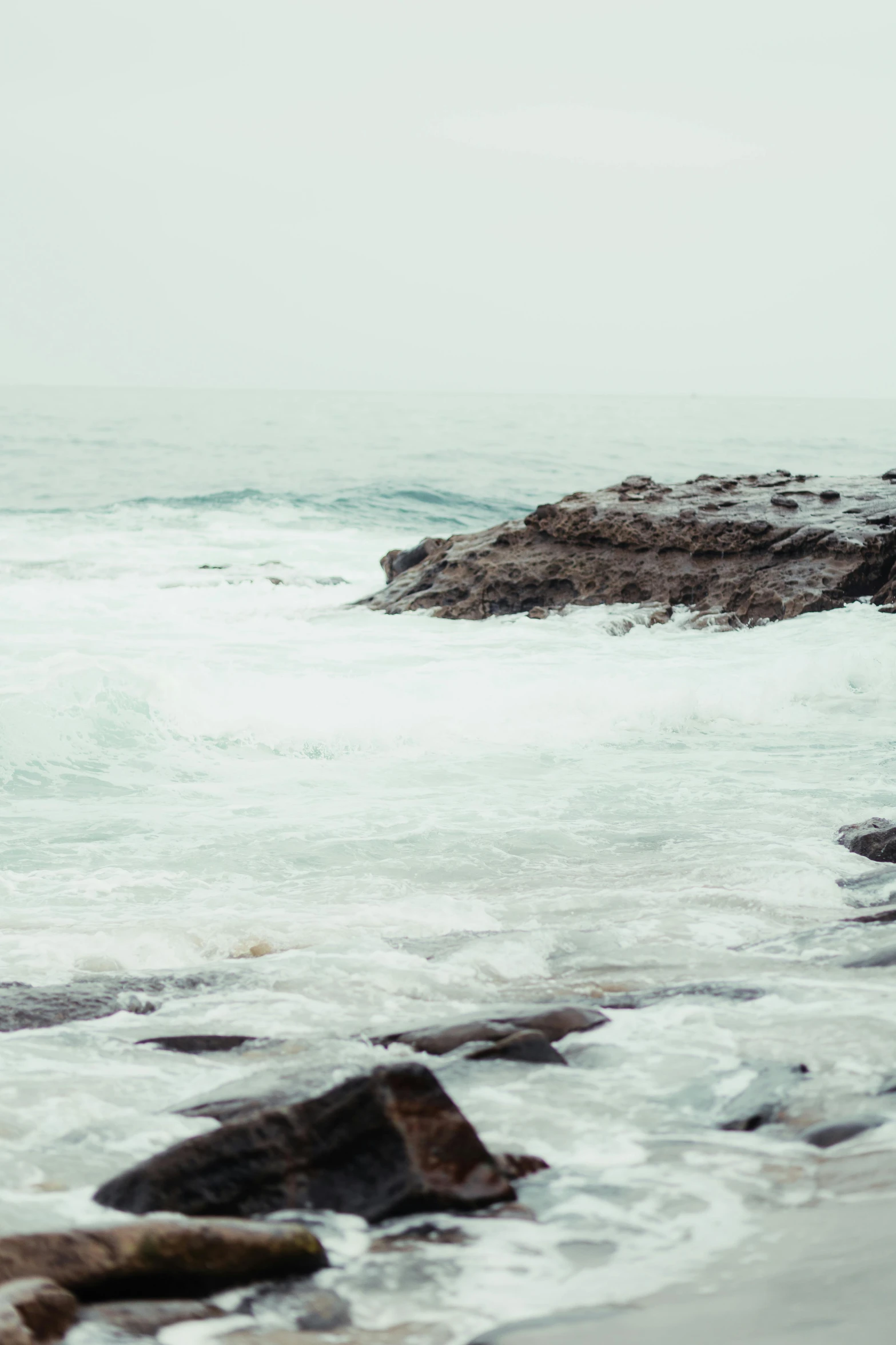 a man standing on top of a rocky beach next to the ocean, inspired by Elsa Bleda, trending on unsplash, minimalism, rushing water, hd footage, white water, overcast day