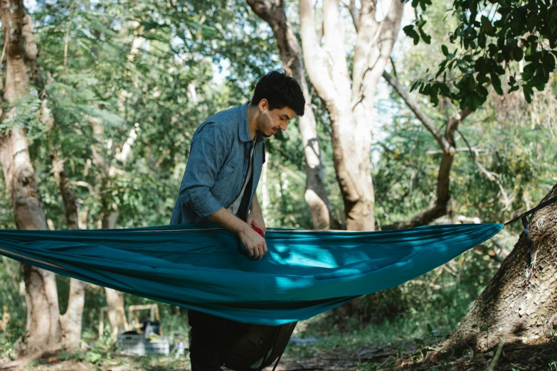 a man holding onto a hammock in the woods, happening, teal cloth, tamborine, thumbnail, exterior shot