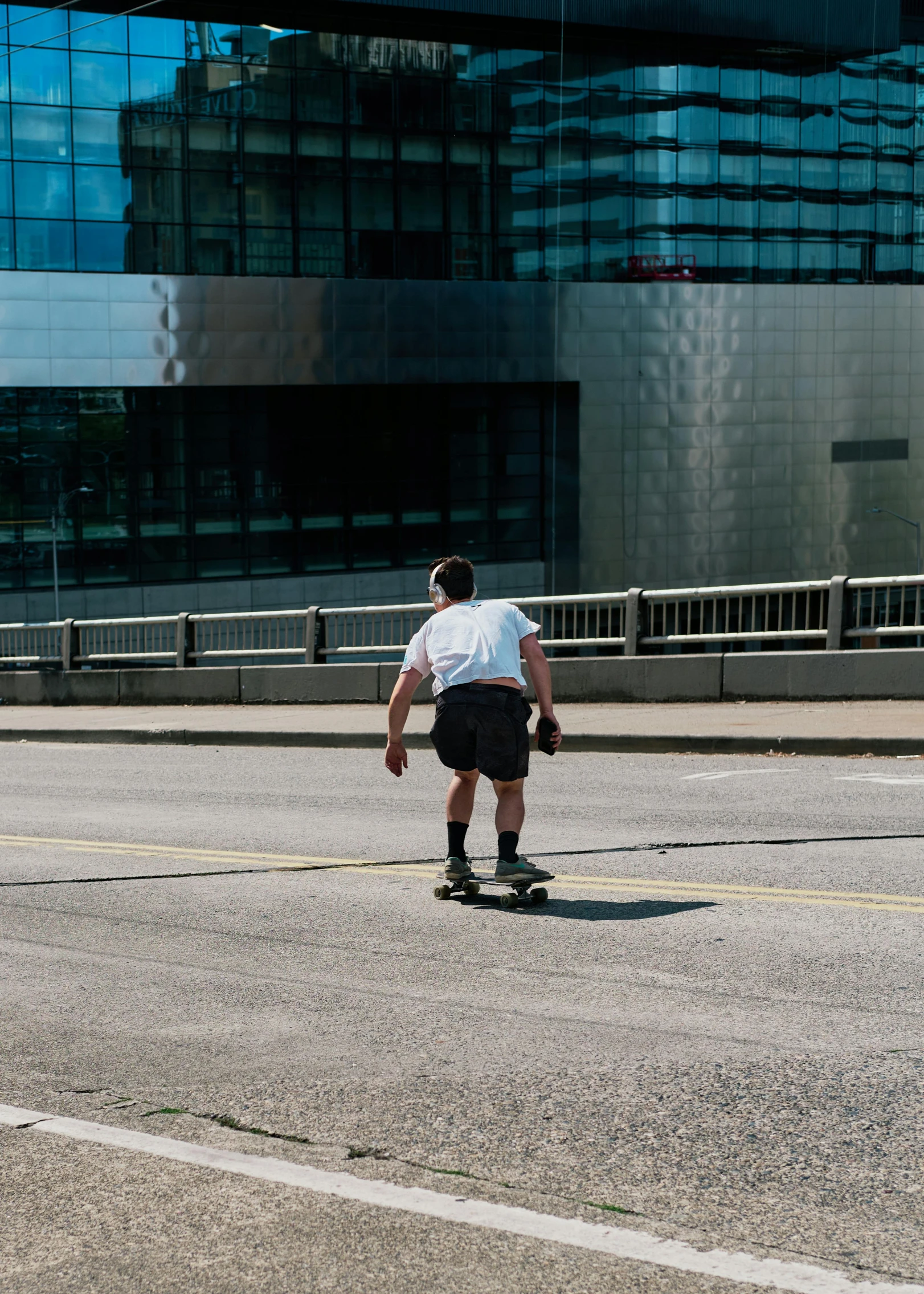 a man riding a skateboard down a street, by Daniel Seghers, pittsburgh, wearing shorts and t shirt, toronto, with his back turned
